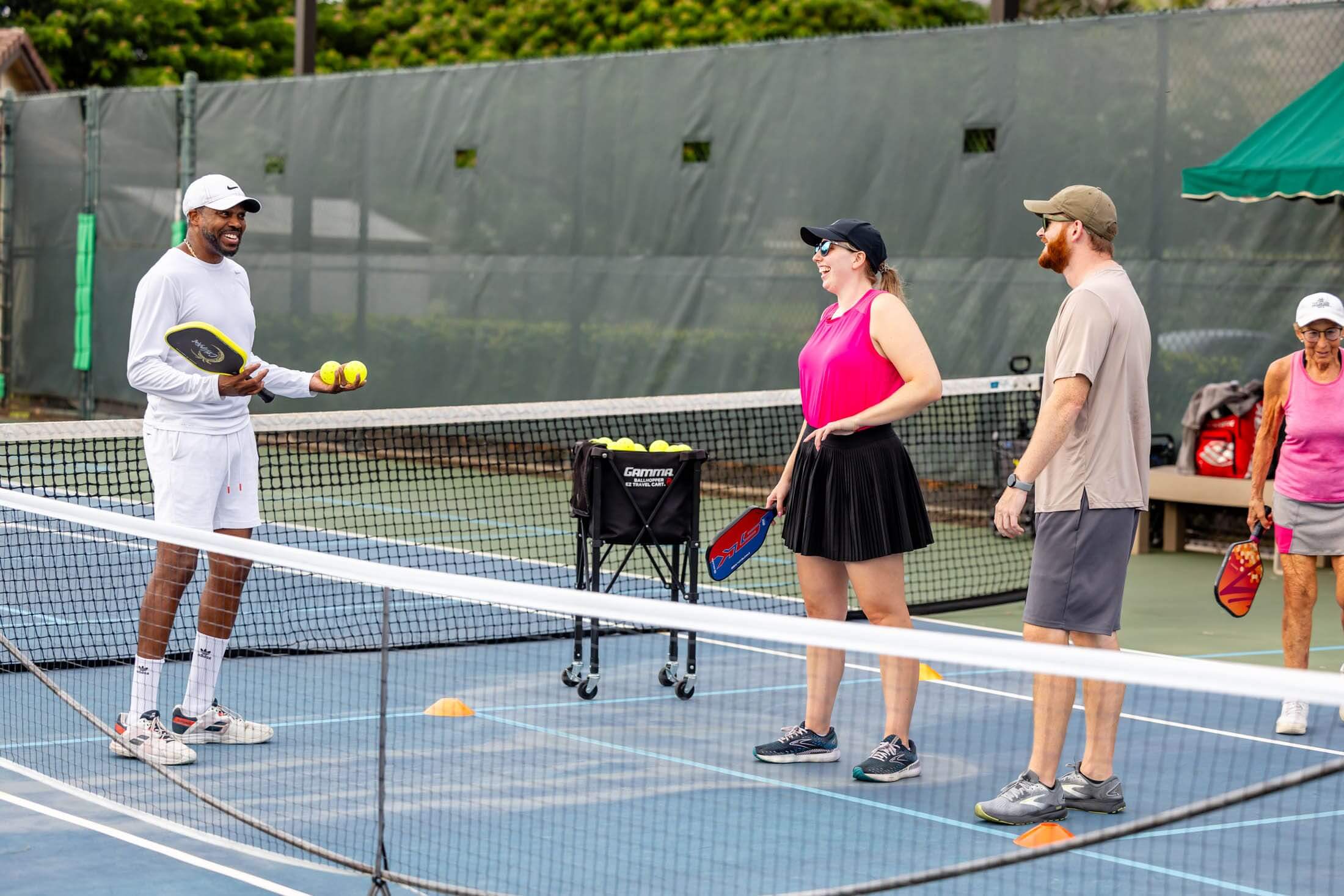 Two adults and a coach on a tennis court during a lesson.
