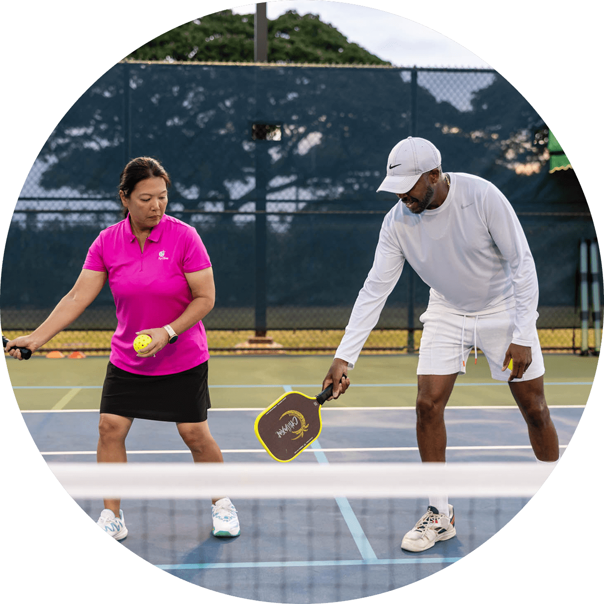 Two people playing pickleball on an outdoor court, one in pink and the other in white.
