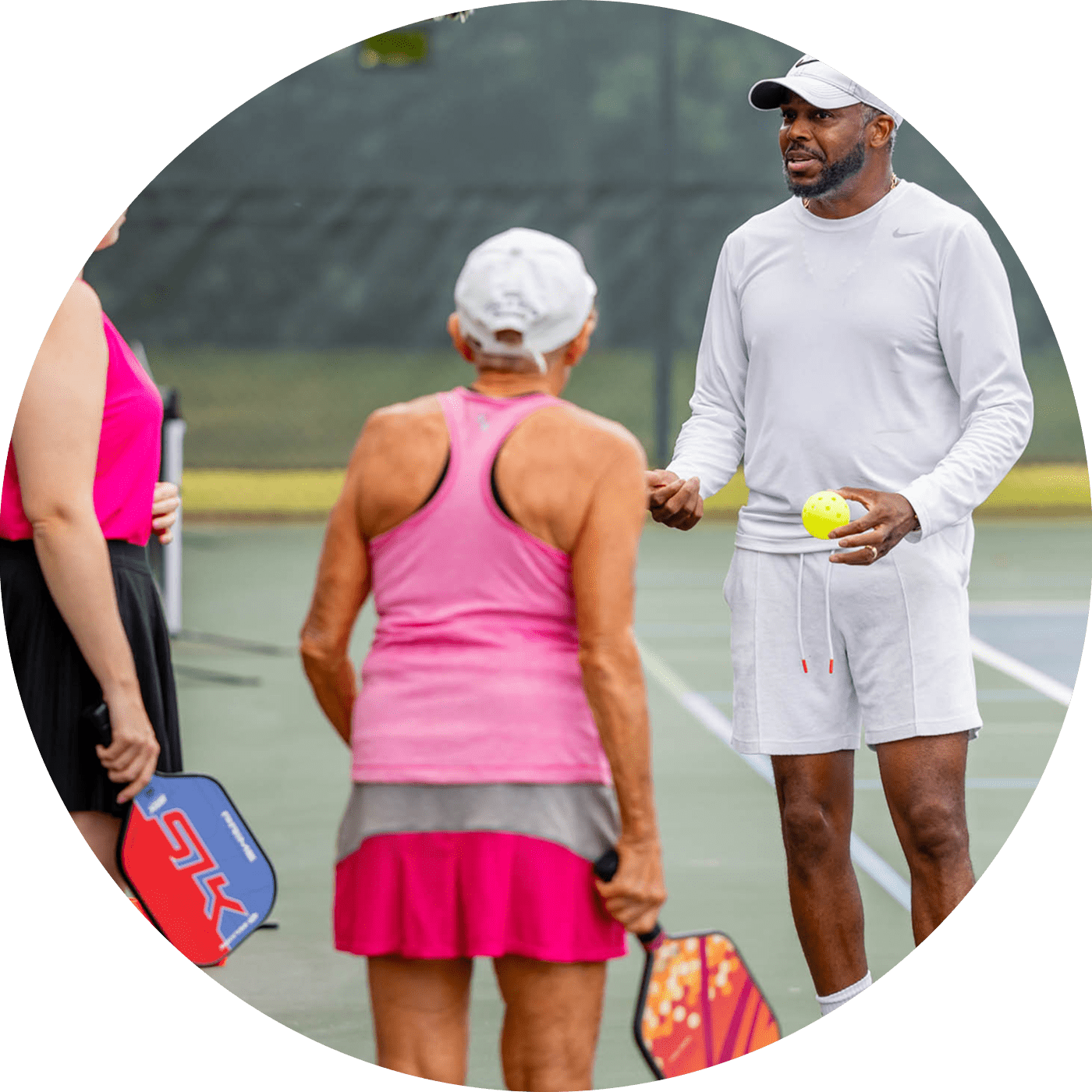 Three people standing on a paddle tennis court with paddles.